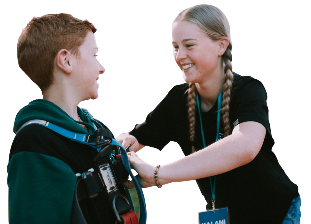 Stoke gap year girl helping holiday camp student with harness on adventure activity.